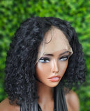 Black curly wig on a mannequin head with a green leafy background