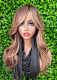 Mannequin head with long, wavy hair against a green leafy background