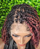 Mannequin head with a wig featuring black and red ombre braids against a green leafy background.