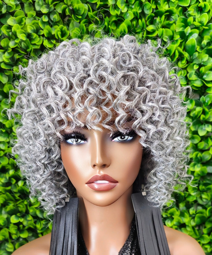 Mannequin head with gray curly wig against a green leafy background